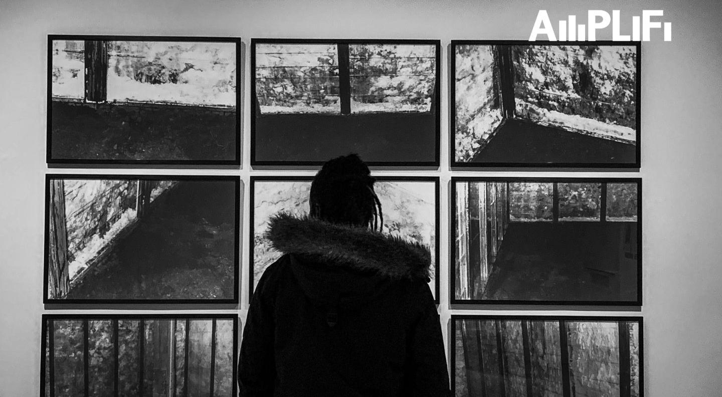 A black silhouette of a man, standing in front of nine black and white images of landscapes and trees