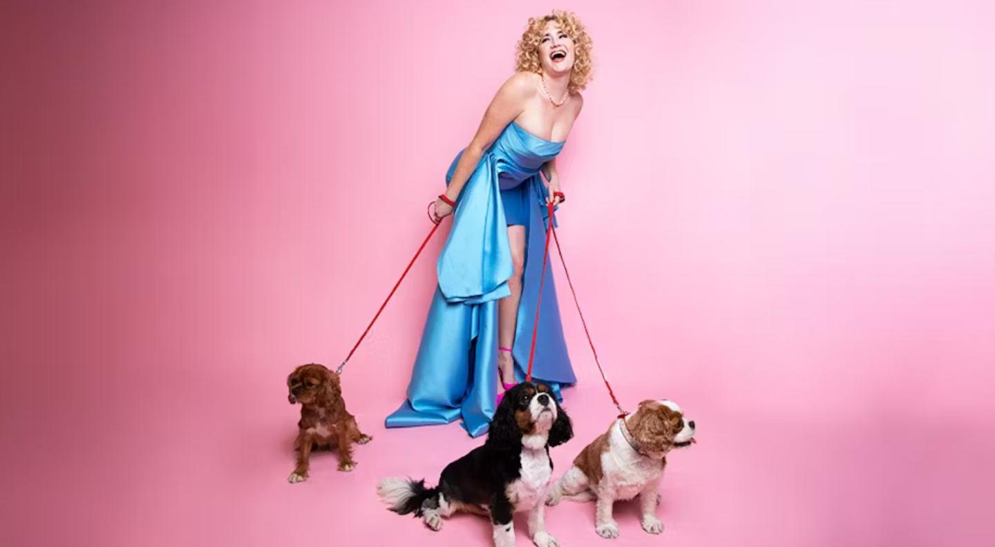 Grace Campbell, a woman with curly blonde hair wearing a long blue evening gown, laughs as she holds the leashes of several dogs