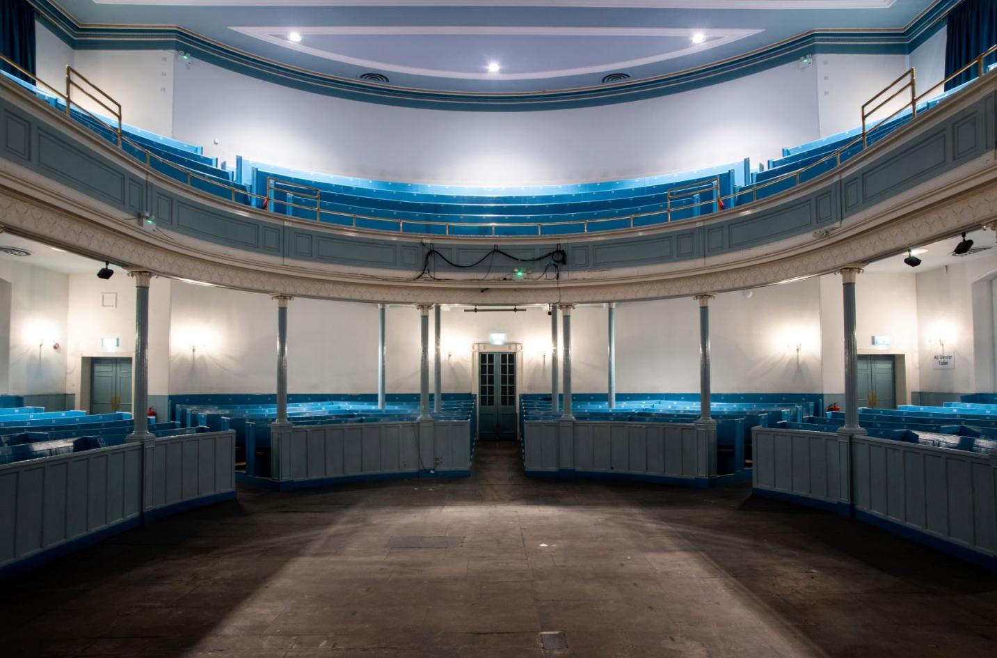 A view of curved blue wooden seating across two levels and a stone floor