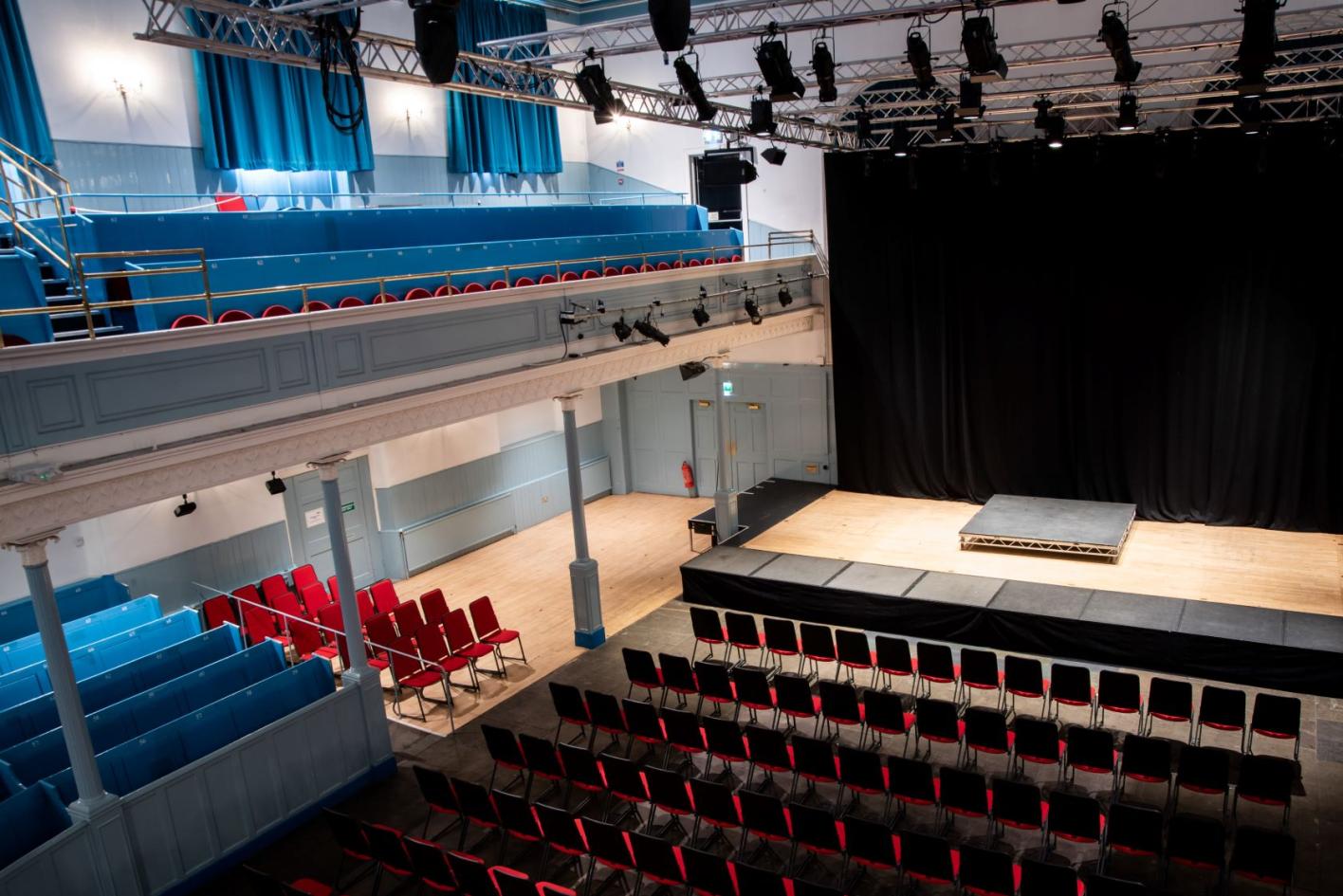 A view from the gallery across to The Queen's Hall stage showing red stall seats and blue pew seating
