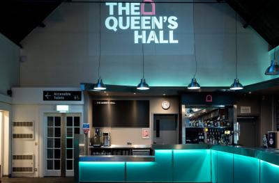 A bar with hanging lights over the top, the Queen's Hall logo above and a sign to Accessible toilets