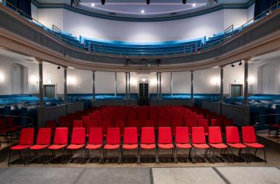 Rows of red chairs with blue wooden seating behind and a gallery above with more seating