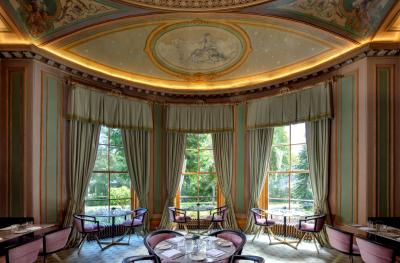 A richly decorated eighteenth century diningroom with gilt decoration on the ceiling and floor to ceiling windows overlooking a garden