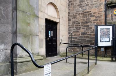 A ramp with a black handrail leads up to a black door with a disabled access sign on it