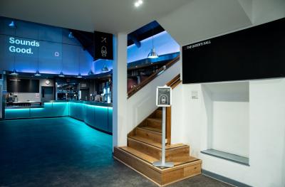 A bar with green lighting and stairs with a sign up to the toilets