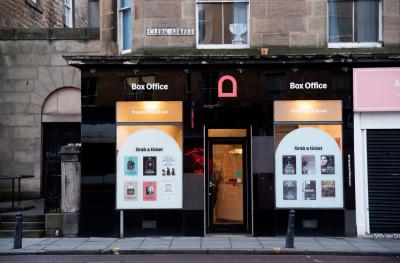 A black fronted building with two large windows with posters in them and a door in the middle