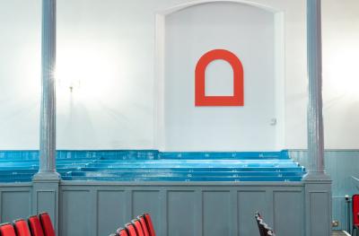 A view of rows of red seats, blue pew seats and a white wall with a red arch