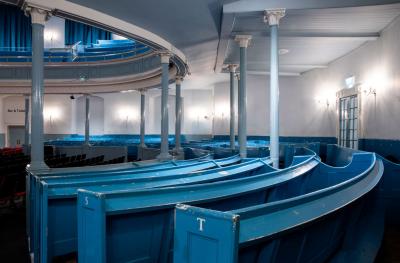 Curved blue wooden pew seating in a room with white walls, light blue columns and bright wall lights