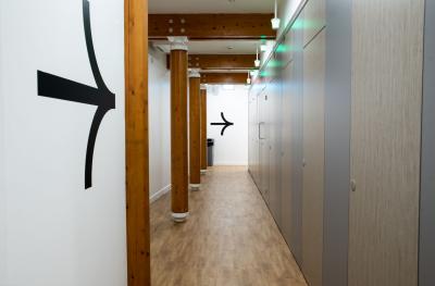 A row of closed toilet cubicles with brown doors, a wooden floor and pillars and a white wall with large black arrows facing away from the camera