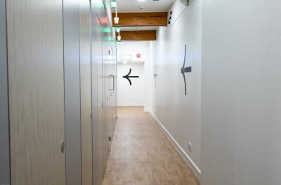 A row of closed toilet cubicles with brown doors, a wooden floor and a white wall with large black arrows facing away from the camera