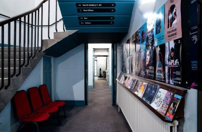 A view of a corridor with poster boards and leaflet racks along one side and stairs going to an upper level on the other