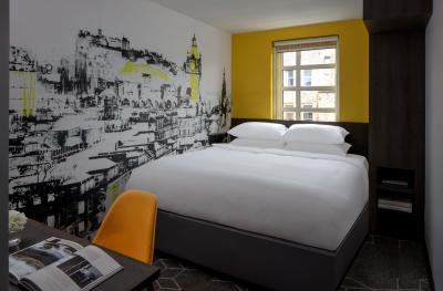 A bedroom with a large bed and desk with one yellow wall and a line drawing of the Edinburgh skyline on another wall