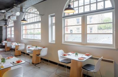 A bright empty dining room with large arched glass windows and small tables laid out for a meal