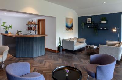 A reception space with wooden flooring, blue velvet chairs, tables and a bar