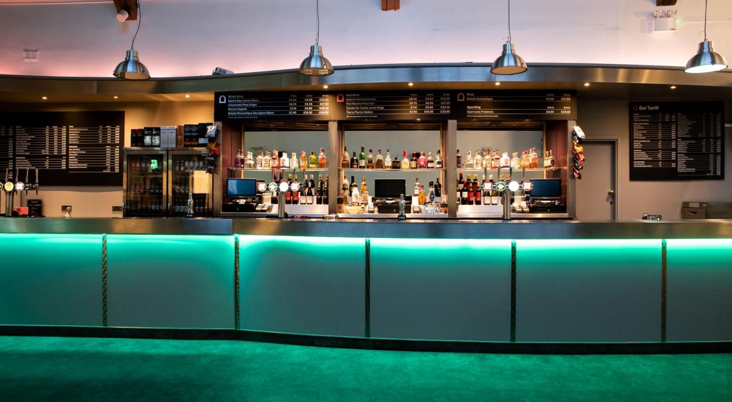 A brightly coloured bar with lots of bottles, mirrors, fridges, beer taps and price lists