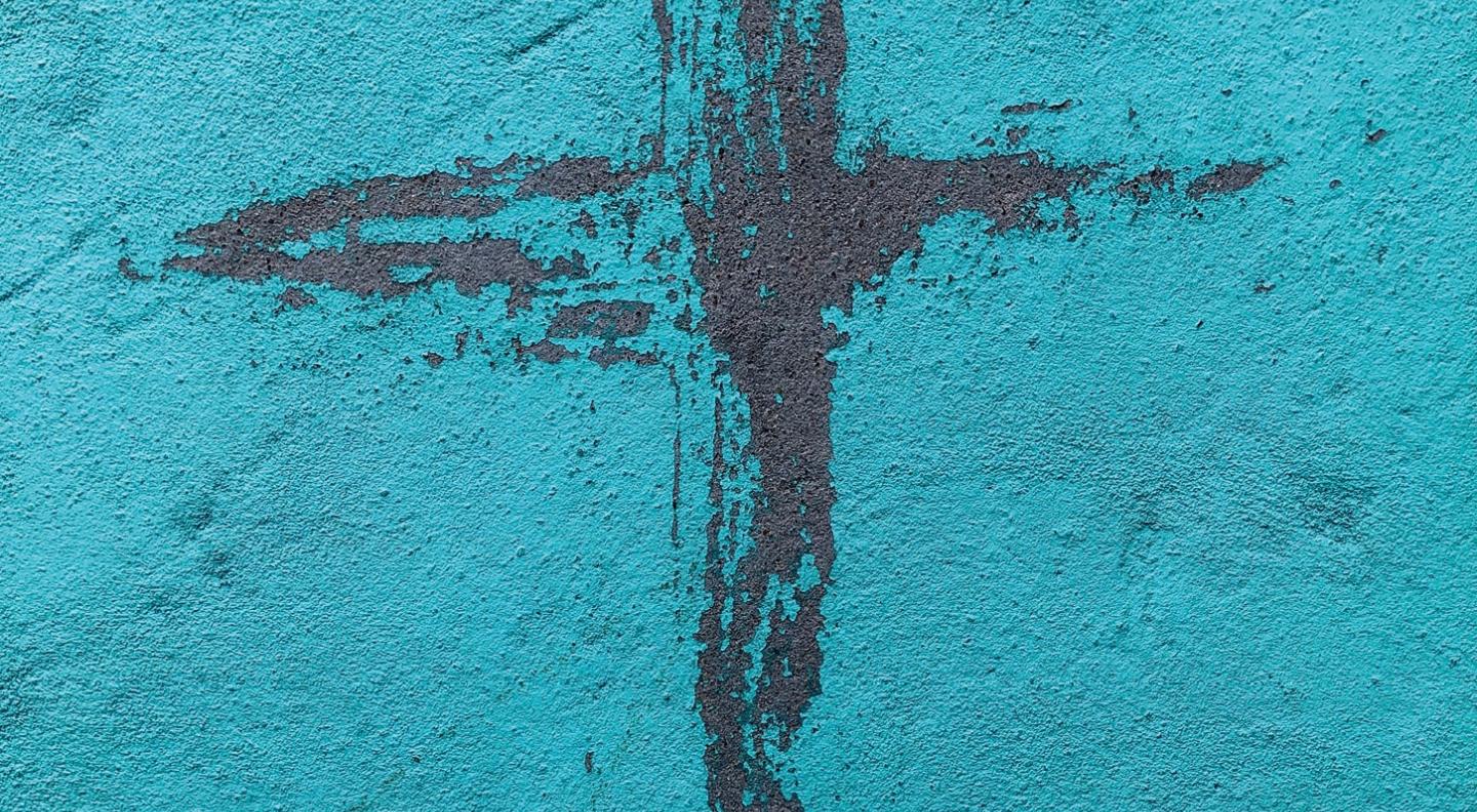 A crude crucifix scratched into green paint on a textured wall