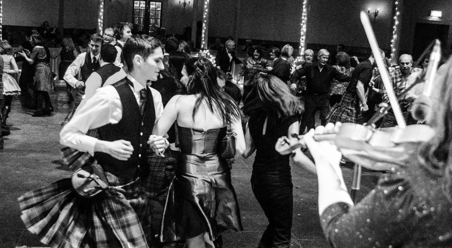 Black and white image of people dressed in evening clothes doing traditional Scottish dancing at The Queen's Hall to celebrate Hogmanay