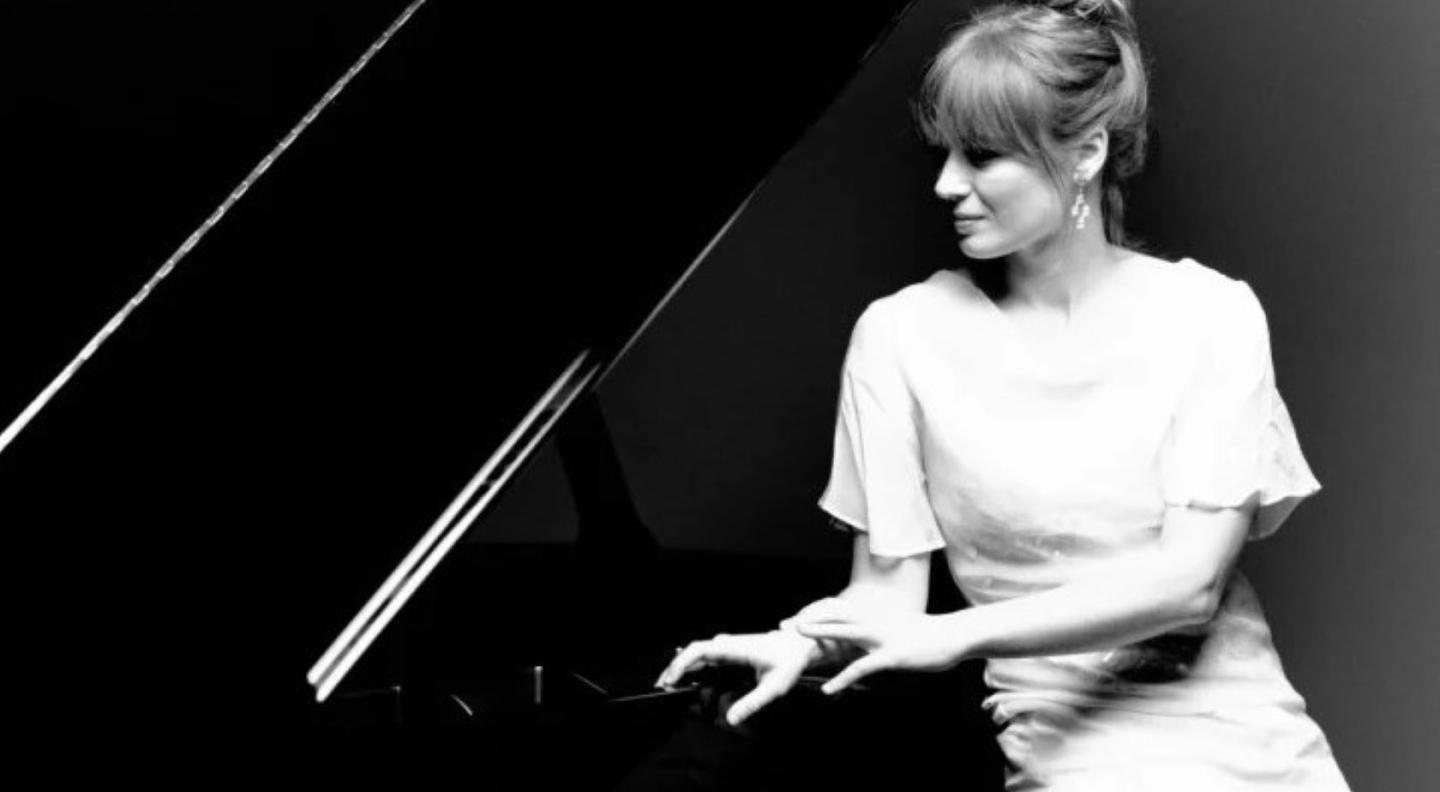 A black and white photo of a white woman leaning on a piano