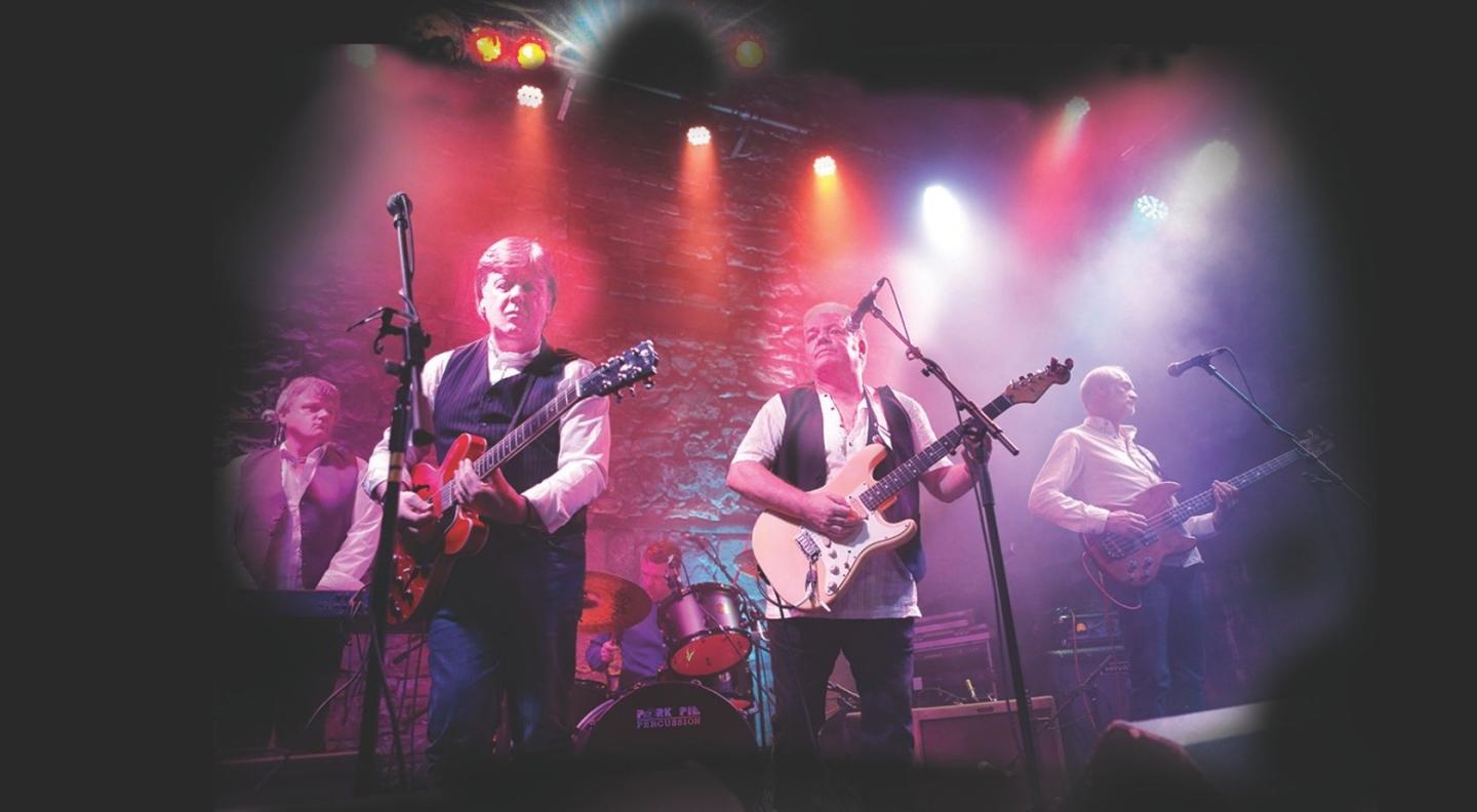 A rock band playing instruments on stage in a reddish haze