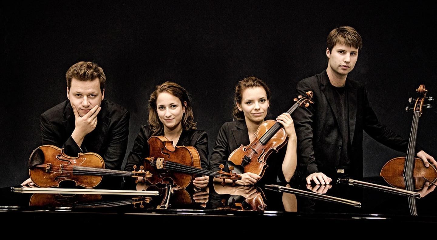 The quartet sit with their instruments against a black background