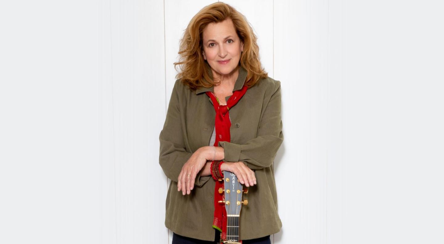 Barbara Dickson posing with her guitar in front of a white background