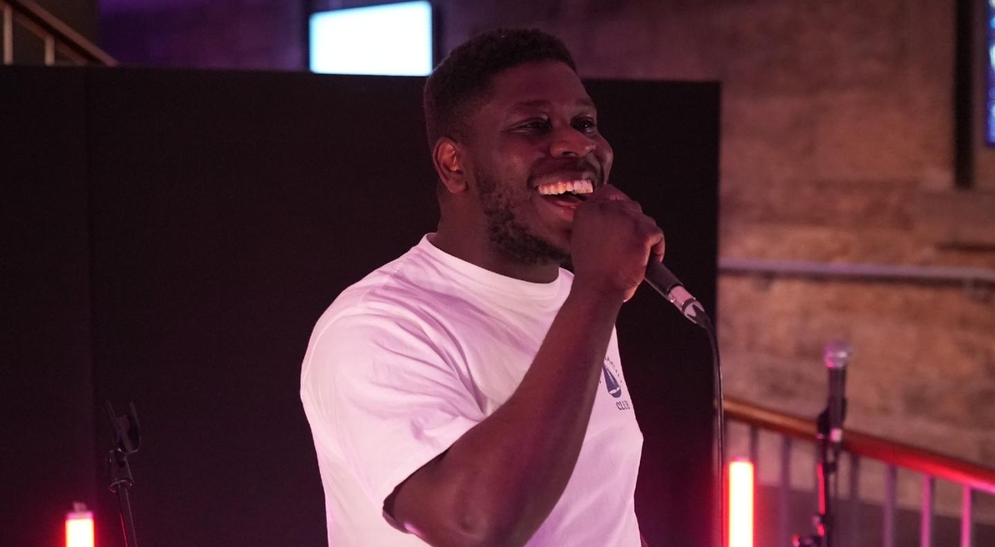 Bemz a young black man wearing a white tshirt sings into a microphone