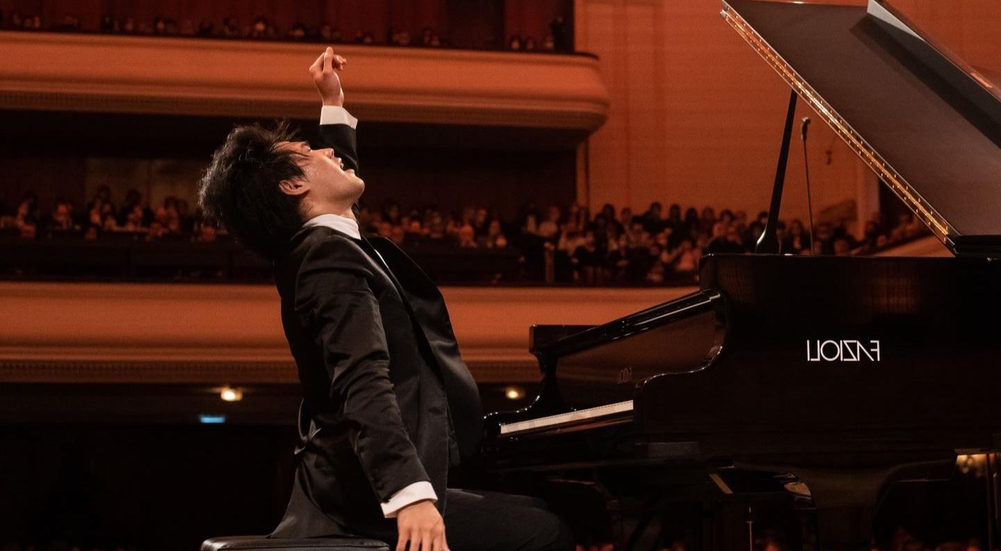 Brue Liu, sat at a piano, makes a grand flourish with his hand