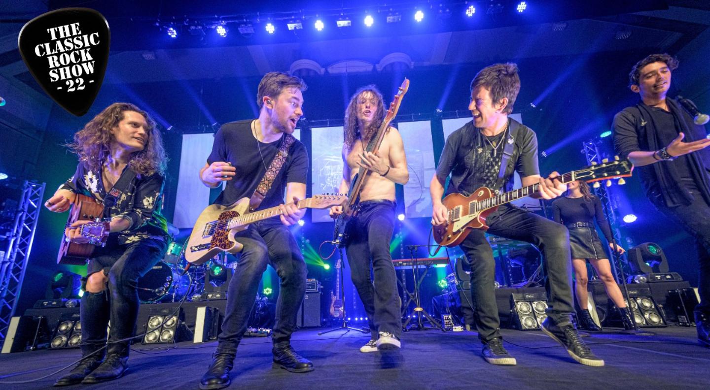 Five members of the Classic Rock Show stand at the front of a stage playing guitar