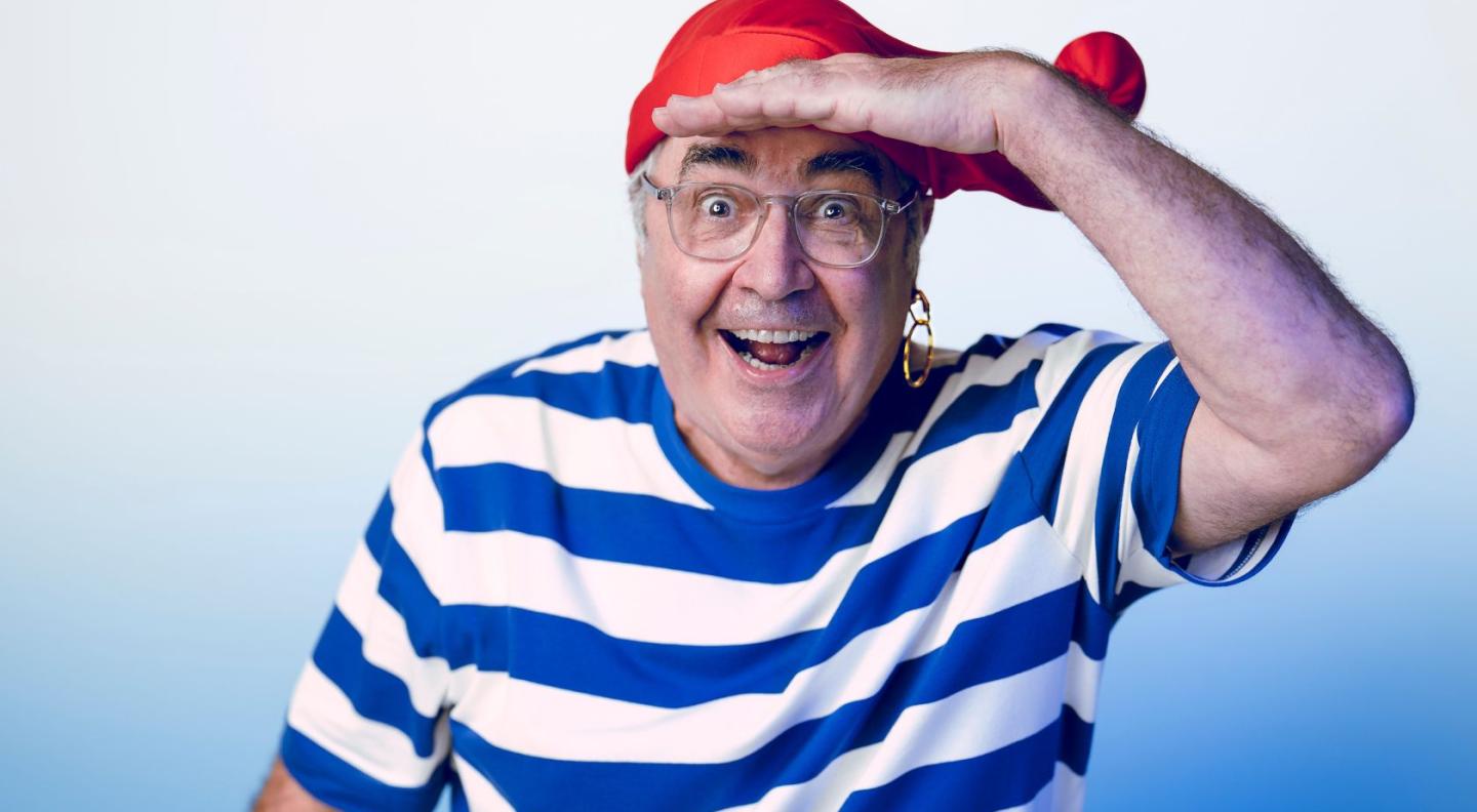 Danny Baker smiling at the camera wearing a blue and white striped t-shirt and red headscarf