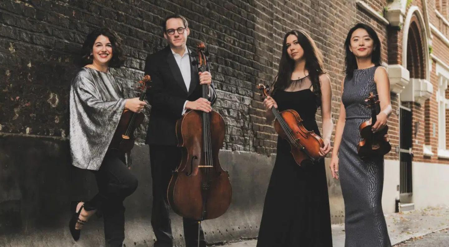 The four members of the Doric String Quartet, three women and one man, standing in a row holding their instruments