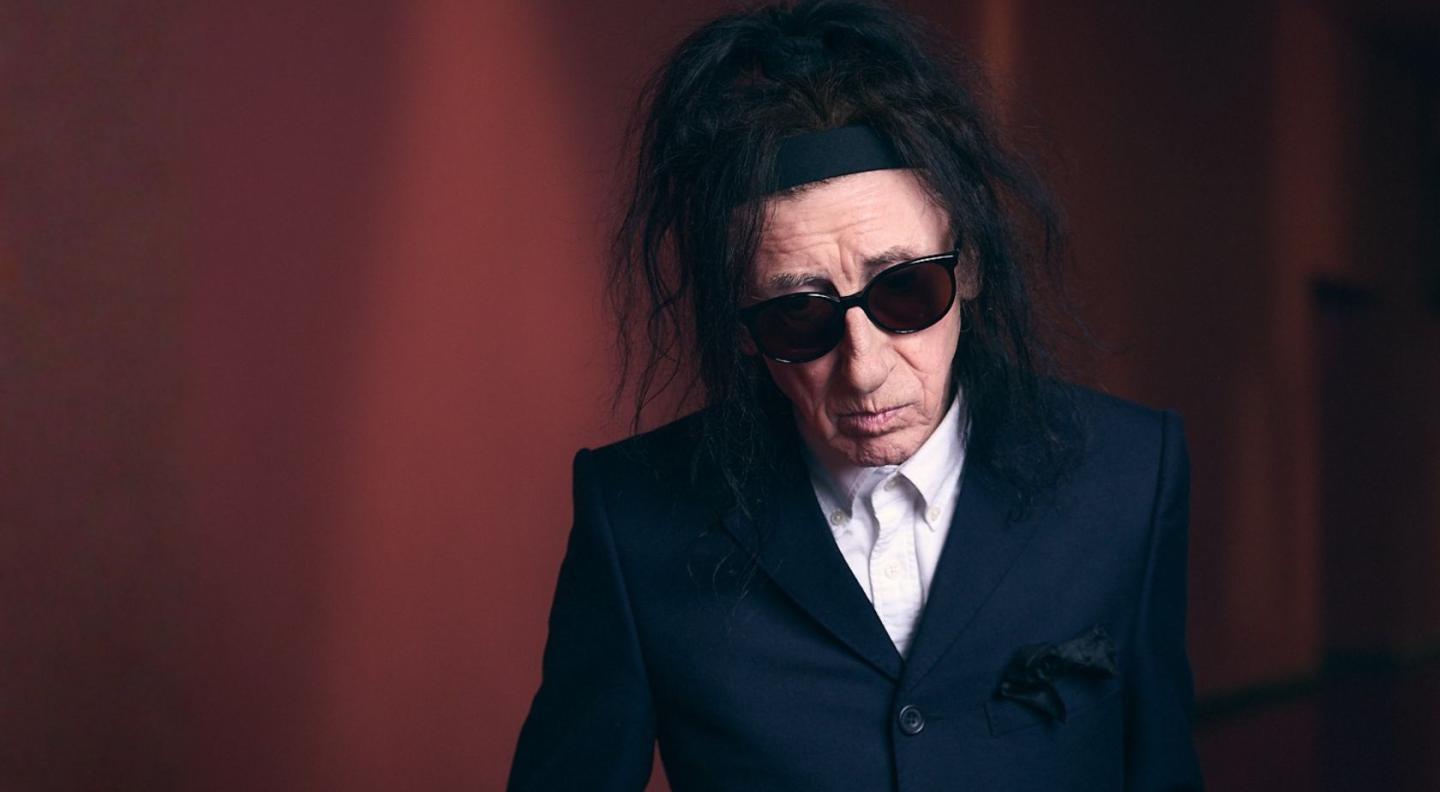 dr-john-cooper-clarke-in-sunglasses-against-a-red-background