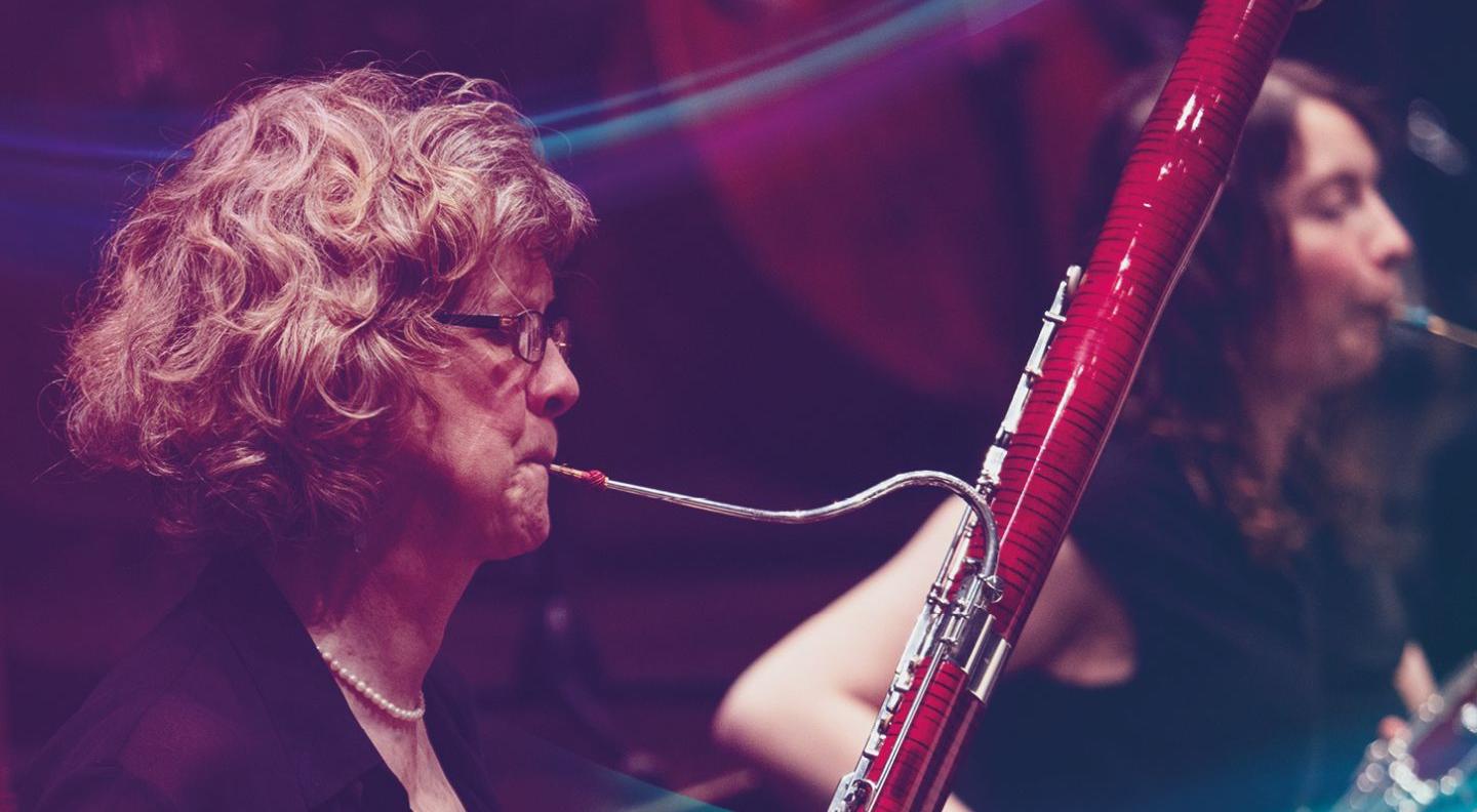 Two female musicians play oboes. The woman in the foreground has curly blonde hair and glasses.