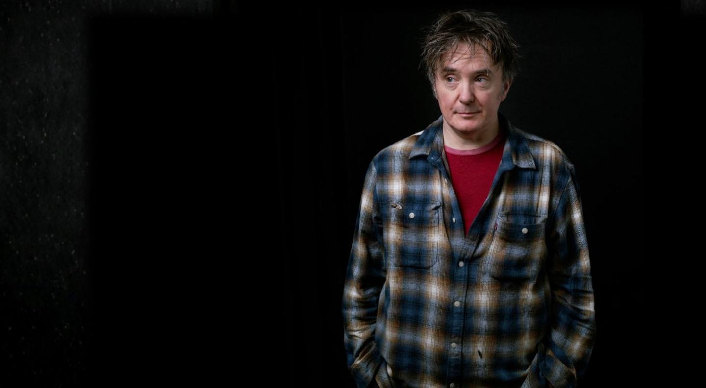 Dylan Moran standing against a black background