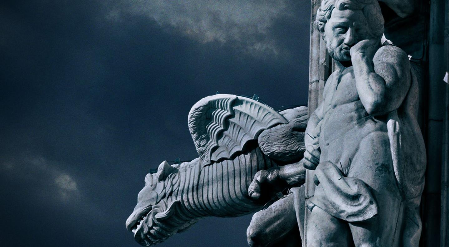 Stone carvings of a figure and a dragons head against a background of the sky.