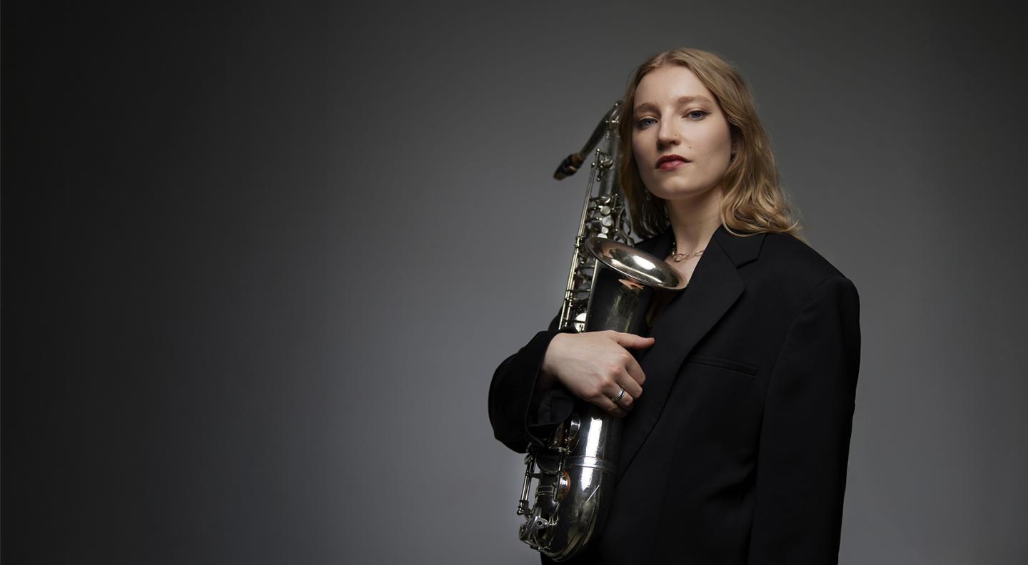 Emma Rawicz in a black suit cradling a saxophone to her chest