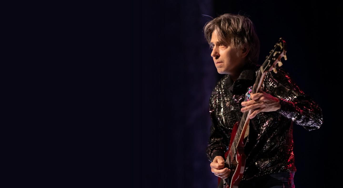 Eric Johnson playing the guitar in front of a purple curtain backg