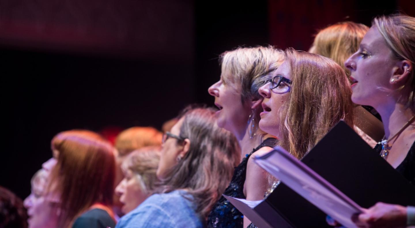 A full colour mid shot of a choir of women singing seen from the side