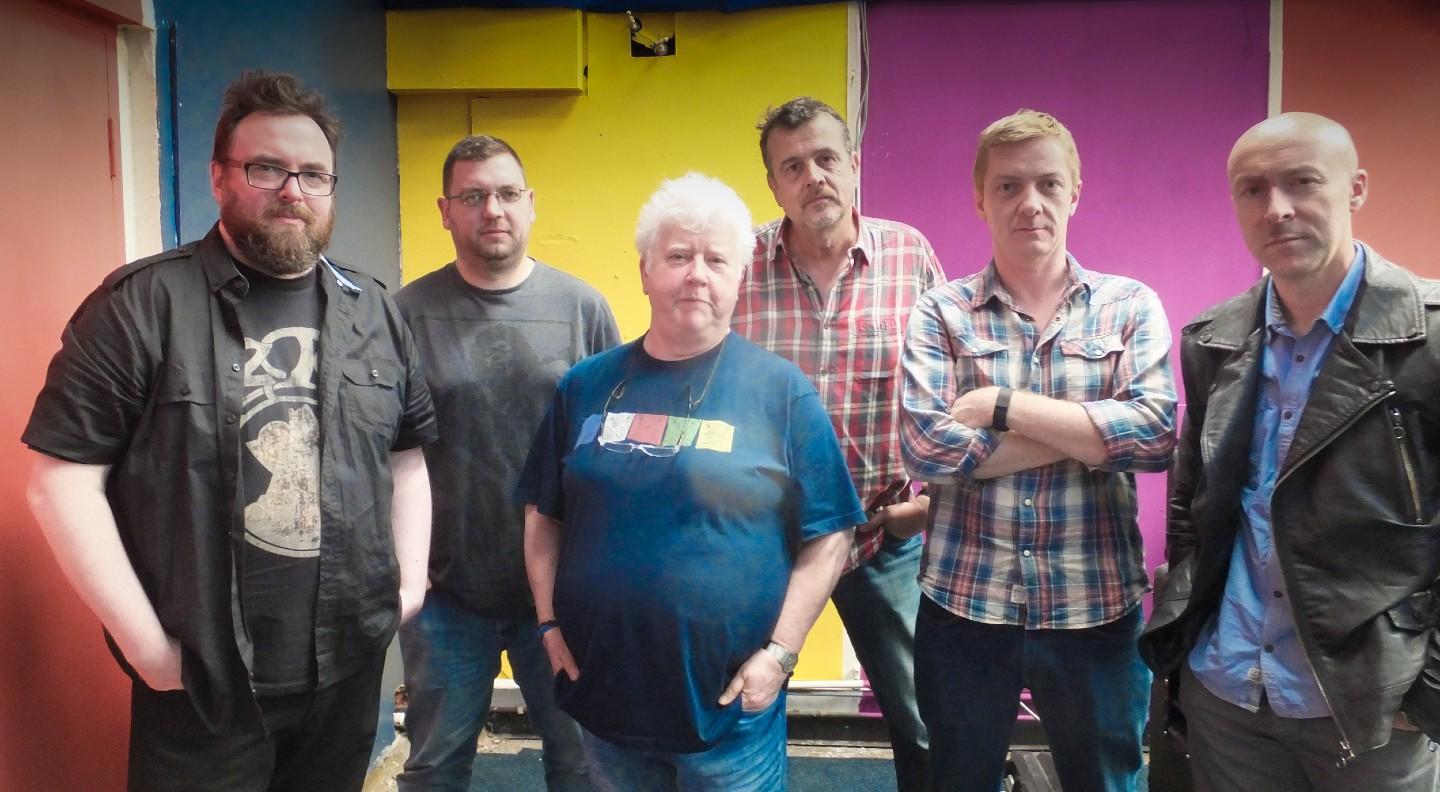 The Fun Lovin' Crime Writers stand in a line casually dressed against a brightly multi-coloured background