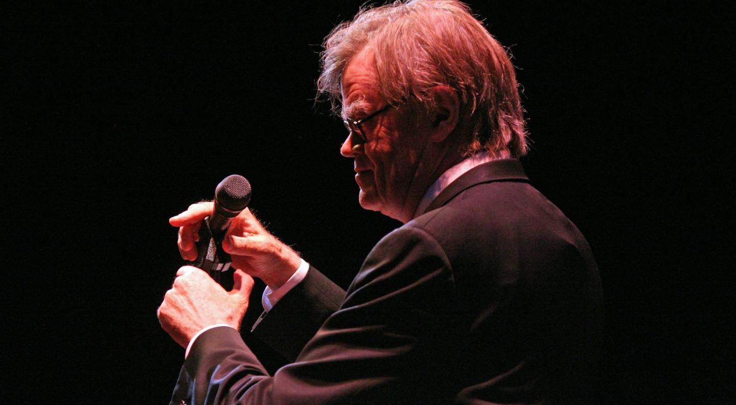 a man alone on a dark stage holding a microphone