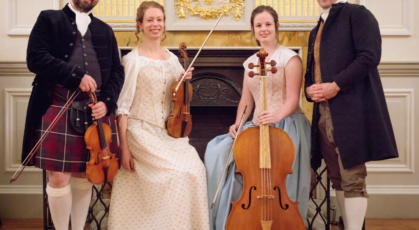 The four members of the Concerto Caledonia in Georgian dress standing in front of a grand fireplace