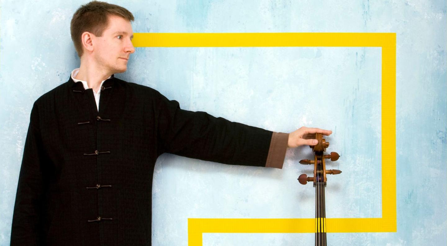 Jonathan Manson posing with his hand on the top of a cello