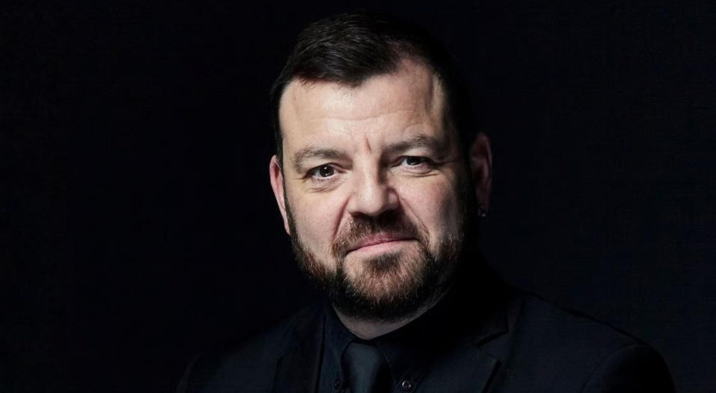 Steven Devine in a black suit against a black background