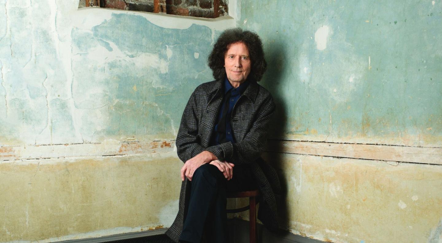 Gilbert O'Sullivan sits in the corner of a room with faded blue paint