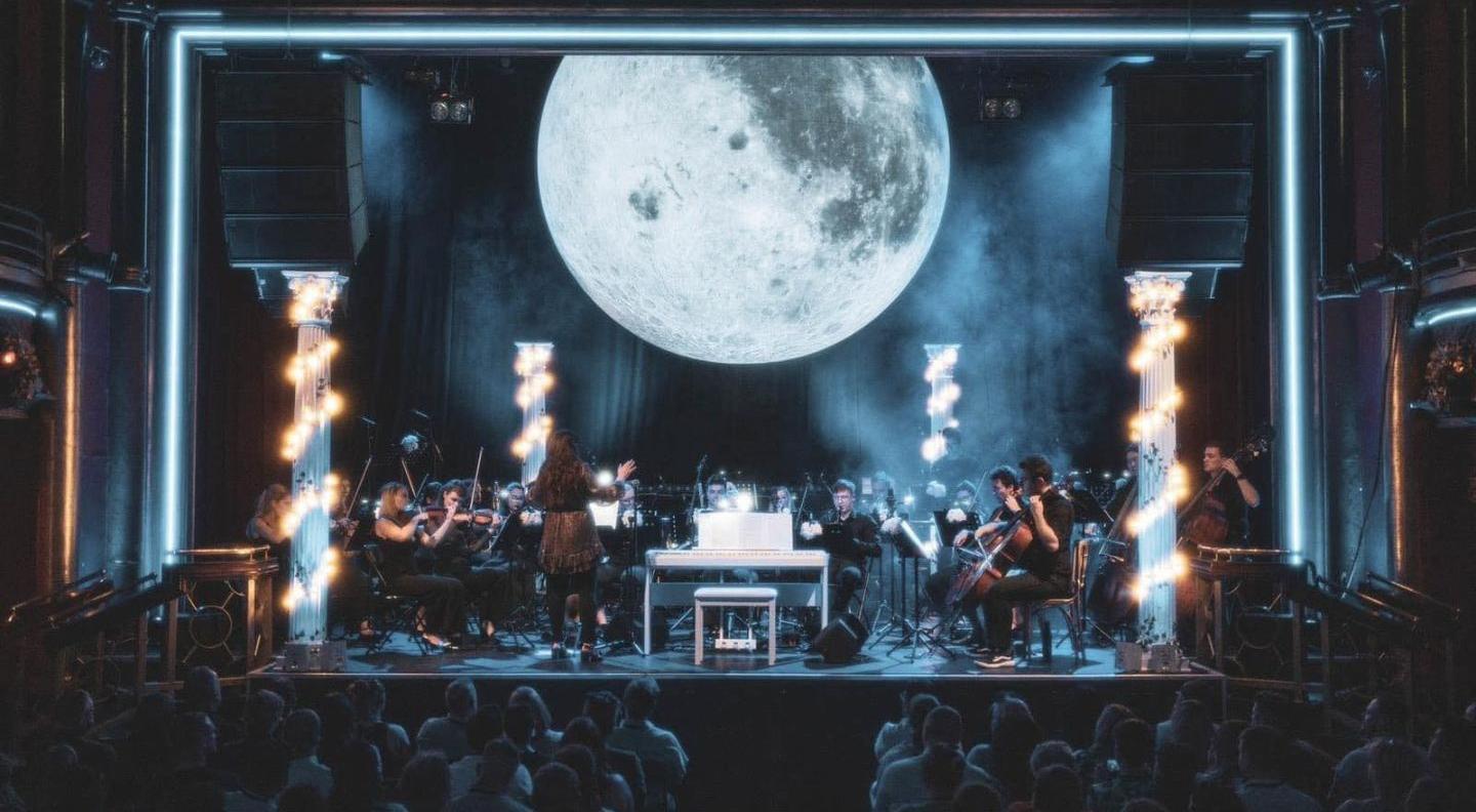An orchestra playing on a stage under a large moon