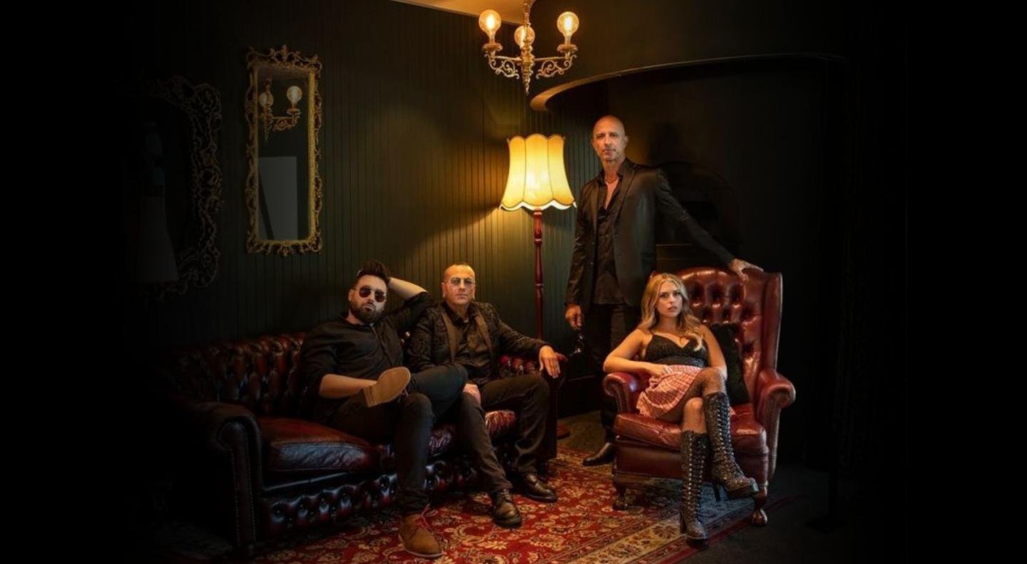The four members of Hindley Street Social Club, three men and one woman, in a stately room. Two of the men are sitting on a leather sofa, the woman is sitting in a leather armchair, and the remaining man is standing behind the armchair, leaning on it.