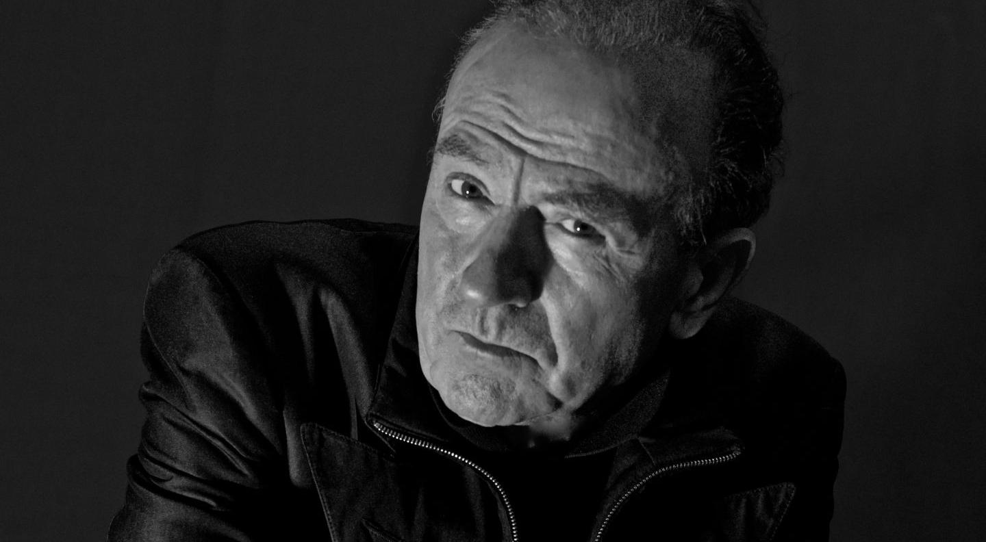 A black and white image of Hugh Cornwell, a white man, wearing a black leather jacker