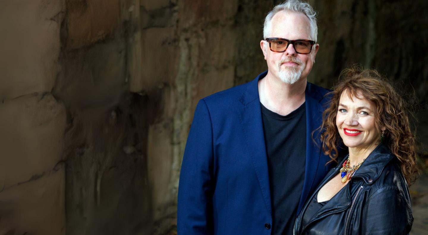 Jacqui Dankworth and Charlie Wood standing in front of a stone wall.