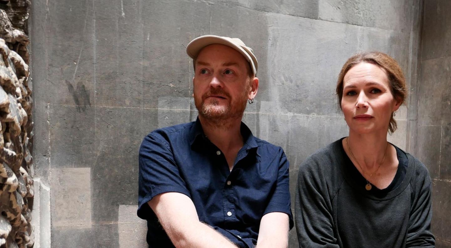 James Yorkston and Nina Persson sitting in front of a grey brick wall