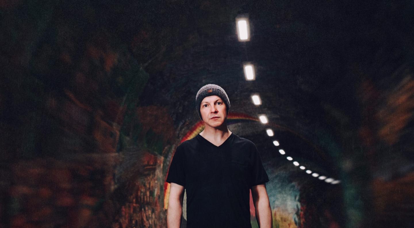 John McCusker stands in a dimply lit tunnel, wearing a beanie hat