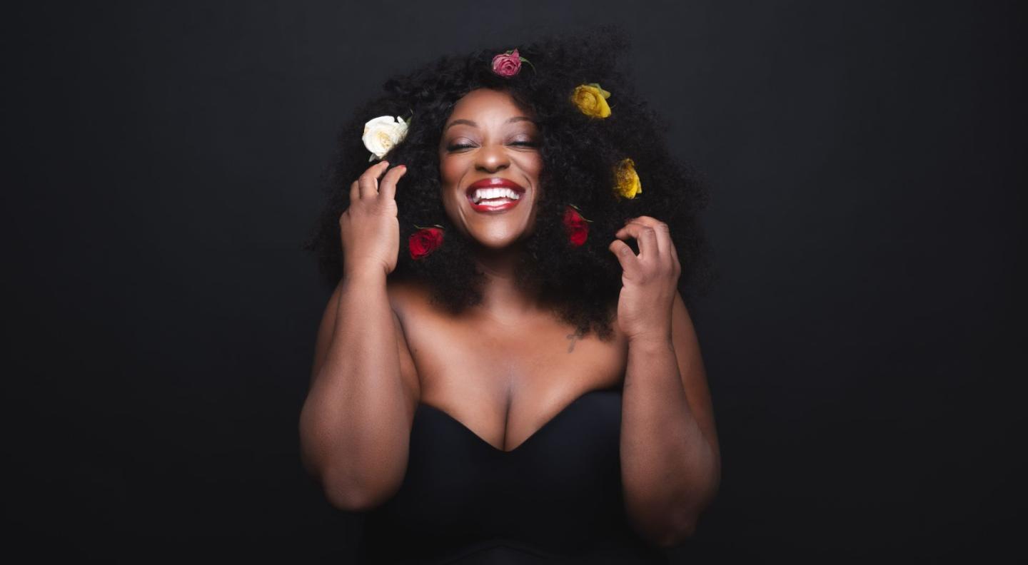 Judi Love with flowers around her head smiling at the camera